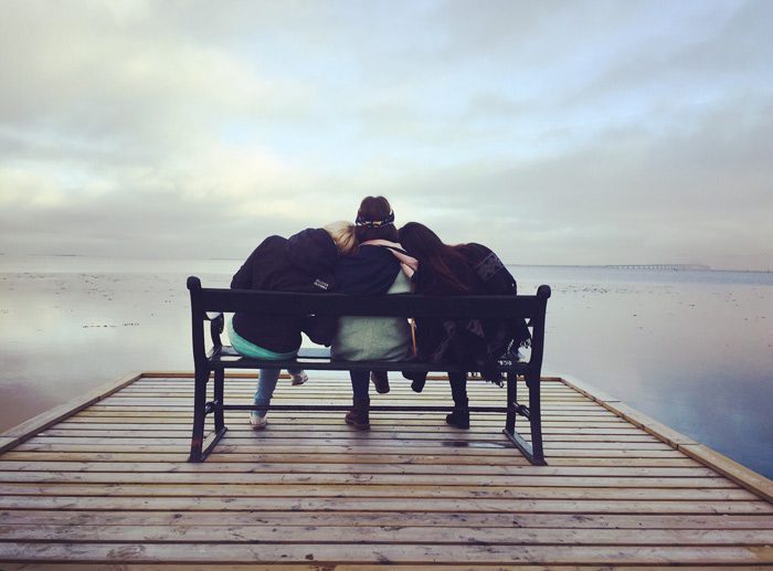 three friends sitting closely on bench on pier - drinking problem