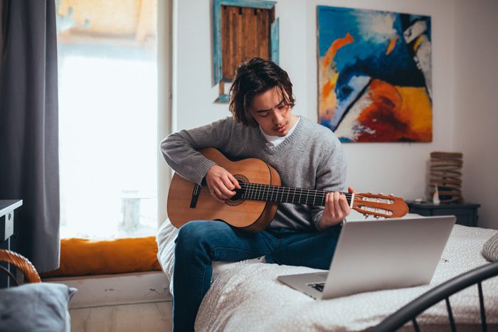 young man sitting in room practicing guitar - creative side
