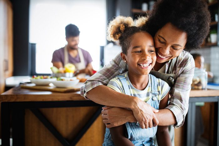 beautiful Black family - smiling mom hugging young daughter from behind in the kitchen