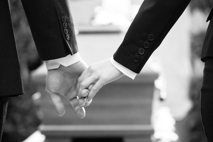 black and white image of two people holding hands in front of a casket - overdose