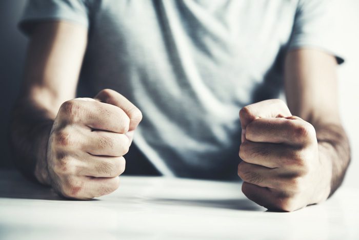 cropped shot of person sitting at a table with their clenched fists resting on the table top - anger