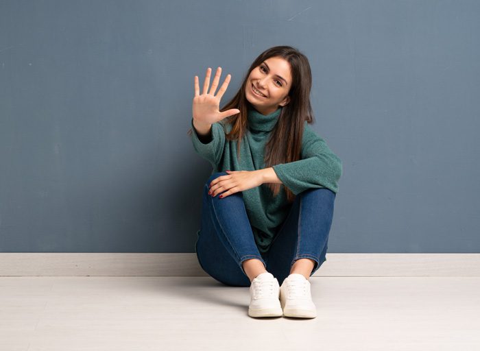 pretty young brunette woman sitting on the ground holding her hand out to signal the number five - myth