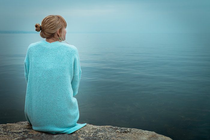 woman sitting at the edge of a lake with her back to the camera - lovely blue tones - PTSD