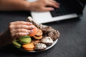 cropped shot of woman's hand getting cookies off of a plate while she uses laptop - sugar addiction
